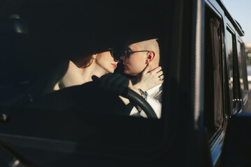 Bride and groom are kissing in a big black car