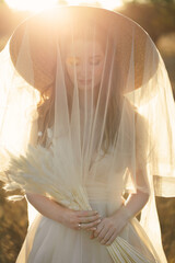 Portrait of a gentle bride in a straw hat and a veil of a veil at sunset