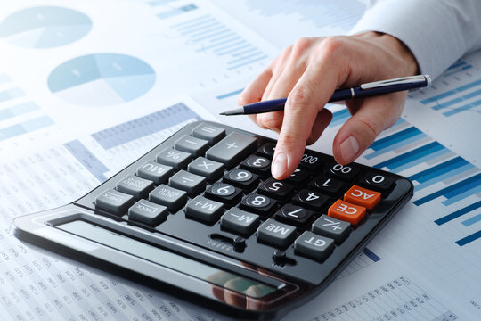 Business person calculating financial data. Close up of hands. Calculator and many reports.