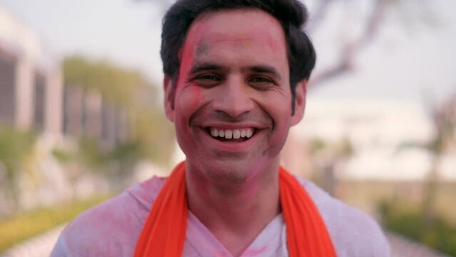 A handsome guy with his face smeared in bright Holi colors posing for the camera - vibrant colors  organic Gulal  dry colors. A young man while celebrating the Indian festival of colors outdoors - ...