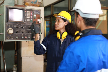 Technician engineer woman in protective uniform with hardhat standing and teaching apprentices or colleague worker to use computerized machine control at heavy industry manufacturing factory