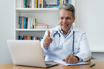 Laughing senior doctor with gray hair with good news for patient at video call