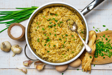 fried chopped cabbage in a frying pan, garlic and green onions, cheese, farm eggs and salt, raw and cooked food in a rustic style on a background of white wooden boards