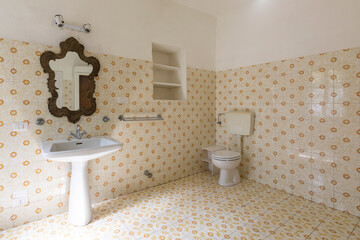 Vintage bathroom in ancient villa with tiles, sink, antique mirror and toilet.