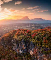 Sonnenuntergang über Bergkette mit buntem Herbstwald auf Hügel in der Landschaft