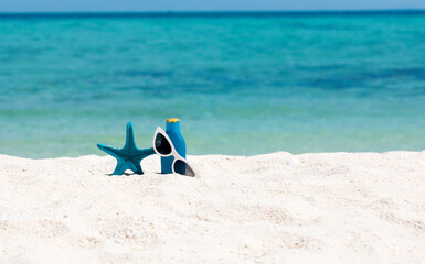 Summer tropical concept with blue starfish ,sunglasses and sunblock bottle on the sand beach background