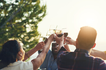 Lets raise them high guys. Shot of a group of friends raising up their glasses for a toast while...