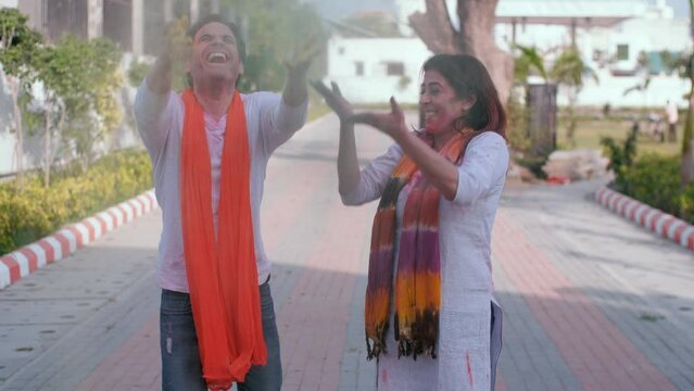 A young Indian husband-wife throwing colors up in the air while celebrating Holi - enjoyment  a Hindu festival  organic Gulal. Best friends wearing traditional clothes dancing together celebrating ...