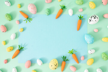 Creative Spring Easter concept on pastel mint background. Painted eggs and carrots with blue copy space for note or invitation. Flat lay.