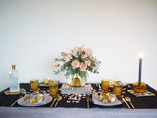 Interesting table decoration with flower styling. Table setting with pastel and golden floral decoration. Pastel colors, golden cutlery, brown glasses and black table cloth.