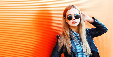 Portrait of stylish blonde young woman in black rock style on vivid background