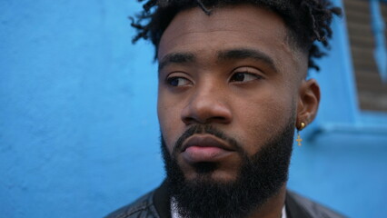 A thoughtful African man leaning on wall outside in street thinking