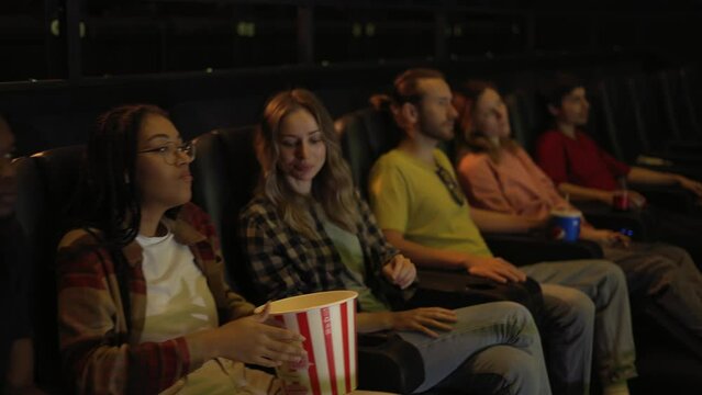 Group of diverse young friends in a movie theater, came watching a movie on a big screen