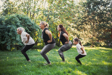 Few generations of one family females squatting doing physical exercises in same way together on...