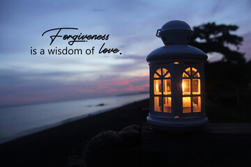 Inspirational quote - Forgiveness is a wisdom of love. With white lantern and the candle light inside on wood in the beach at sunset. Love care, kindness and forgive concept.