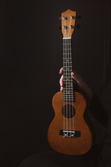 Naklejka premium Musical instrument ukulele in a woman's hand on a dark background