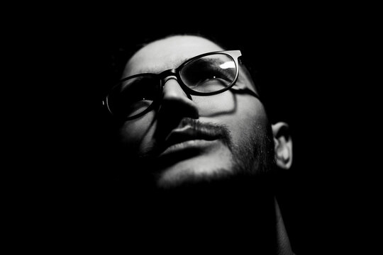 Black and white, close-up dark portrait of young man wearing glasses.