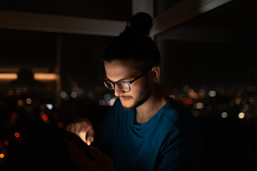 Indoor night portrait of young attractive guy, holding smartphone.