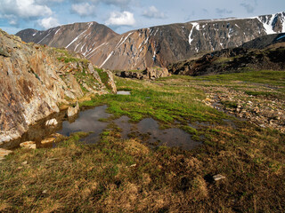 Impressive scenery with puddles on a stony meadow and vast mountains in sunlight. Wet mountain meadow.