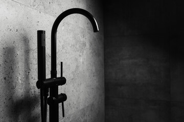 Photo of black floor-standing bath taps, on the background of dark grey wall.