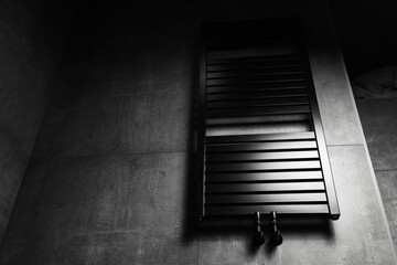 Photo of black matte heated towel rail, in the bathroom with dark grey walls.