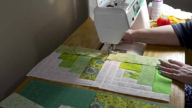 Senior woman using a sewing machine to stitch together quilt blocks