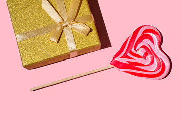 gift  box with bow and heart-shaped lollipop on a pink background. Red and whie striped sweet lollipops. holiday background