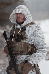 Soldier in winter camouflaged uniform in Modern warfare army on a snow day on forest battlefield...