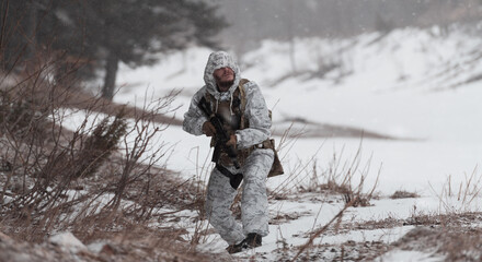 Fototapeta premium Soldier in winter camouflaged uniform in Modern warfare army on a snow day on forest battlefield with a rifle. Model face very similar to Ukraine prime minister.