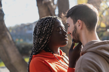 multicultural couple of young people in engaging moment with an African woman touching tenderly her boyfriend chin under the trees in the park - Powered by Adobe