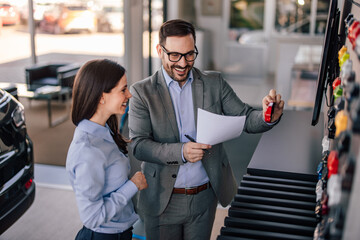 Joyful caucasian man and woman, comparing car prices in the shop