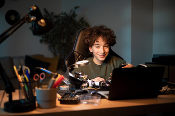 Child spends time at desk in room watching instructional videos on laptop, imitates video makers and solders robot by self, connects wires, creates toy electrical system