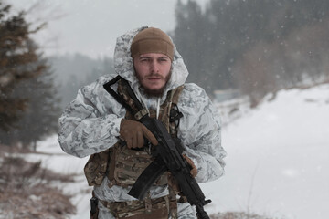 Soldier in winter camouflaged uniform in Modern warfare army on a snow day on forest battlefield...