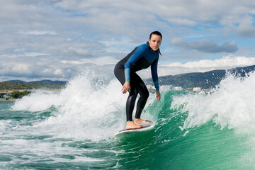 Young athletic female in wetsuit riding on endless waves behind a boat on sunny day. Woman practice wakeboarding, carving behind the baot. Watersport concept.