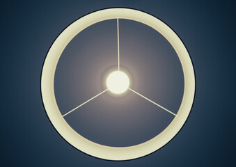 Ring shaped chandelier with three spokes and illuminated lamp in the center. The sconce hanging from the ceiling,  looking like abstract symbol or sci-fi icon. Soft yellow light, dark blue background.