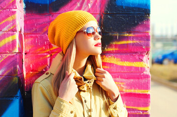 Fashion portrait of beautiful stylish blonde young woman on city street over colorful graffiti background