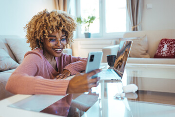 Cheerful african student black woman sitting at table studying using laptop reading a book, take a...