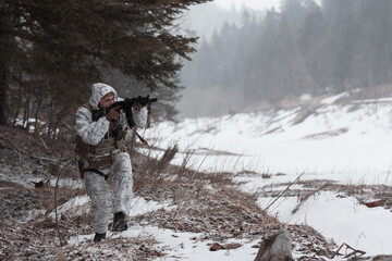 Soldier in winter camouflaged uniform in Modern warfare army on a snow day on forest battlefield...