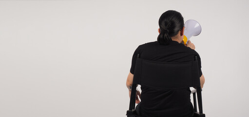 Back of Asian man sitting on black director chair. He holding a megaphone on white...