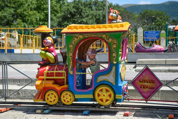 Cute boy rides the railroad on a children's colored locomotive. Children's recreation in an amusement park