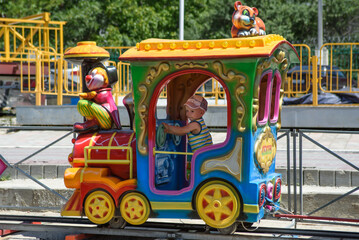 Fototapeta na wymiar Cute boy rides the railroad on a children's colored locomotive. Children's recreation in an amusement park