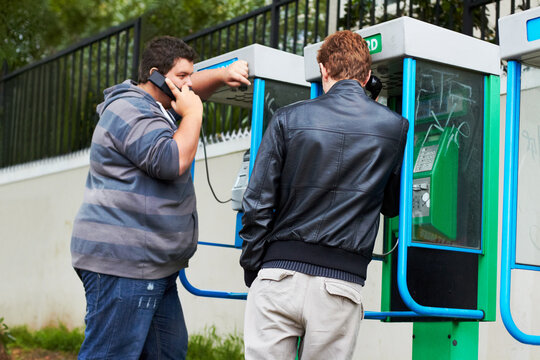 Phoning home. Two young men making phone calls from public pay-phone booths.