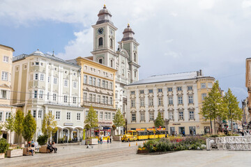 Linz, Austria, 27 August 2021: Baroque Old Cathedral or Alter Dom with two towers, Church of Ignatius, Hauptplatz or main square at sunny summer day, Facade of stone colorful historical buildings