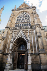 Fototapeta na wymiar Linz, Austria, 27 August 2021: Facade of medieval catholic stone gothic New Cathedral of Immaculate Conception with arch, old town street at sunny summer day, lancet windows and carved statues
