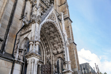 Fototapeta premium Linz, Austria, 27 August 2021: Facade of medieval catholic stone gothic New Cathedral of Immaculate Conception with arch, old town street at sunny summer day, lancet windows and carved statues