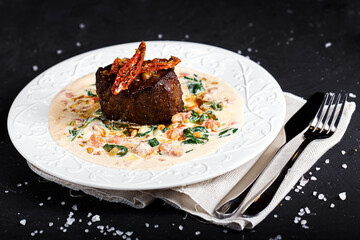 on a white plate, filet mignon with vegetables and cutlery, on a black isolated background
