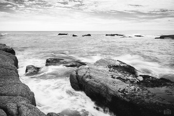 Vista desde rocas en playa oceánica en José Ignacio, Uruguay. Fotografía monocromática,  se aprecia el agua entre rocas en el océano  - obrazy, fototapety, plakaty