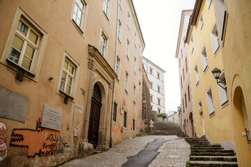 Fototapeta na wymiar Linz, Austria, 29 August 2021: Narrow picturesque street, Facade of colorful buildings in historic center of medieval city, renaissance and baroque houses at summer sunny day, stairs, wooden windows