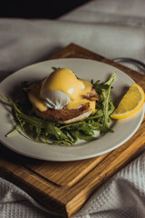 Eggs benedict and poached hollandaise sauce with arugula and lemon. Delicious food for breakfast. High quality photo