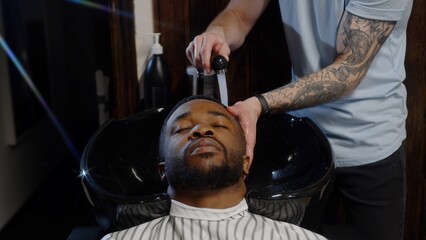Barber washes shampoo off the head of an African American in a special sink
